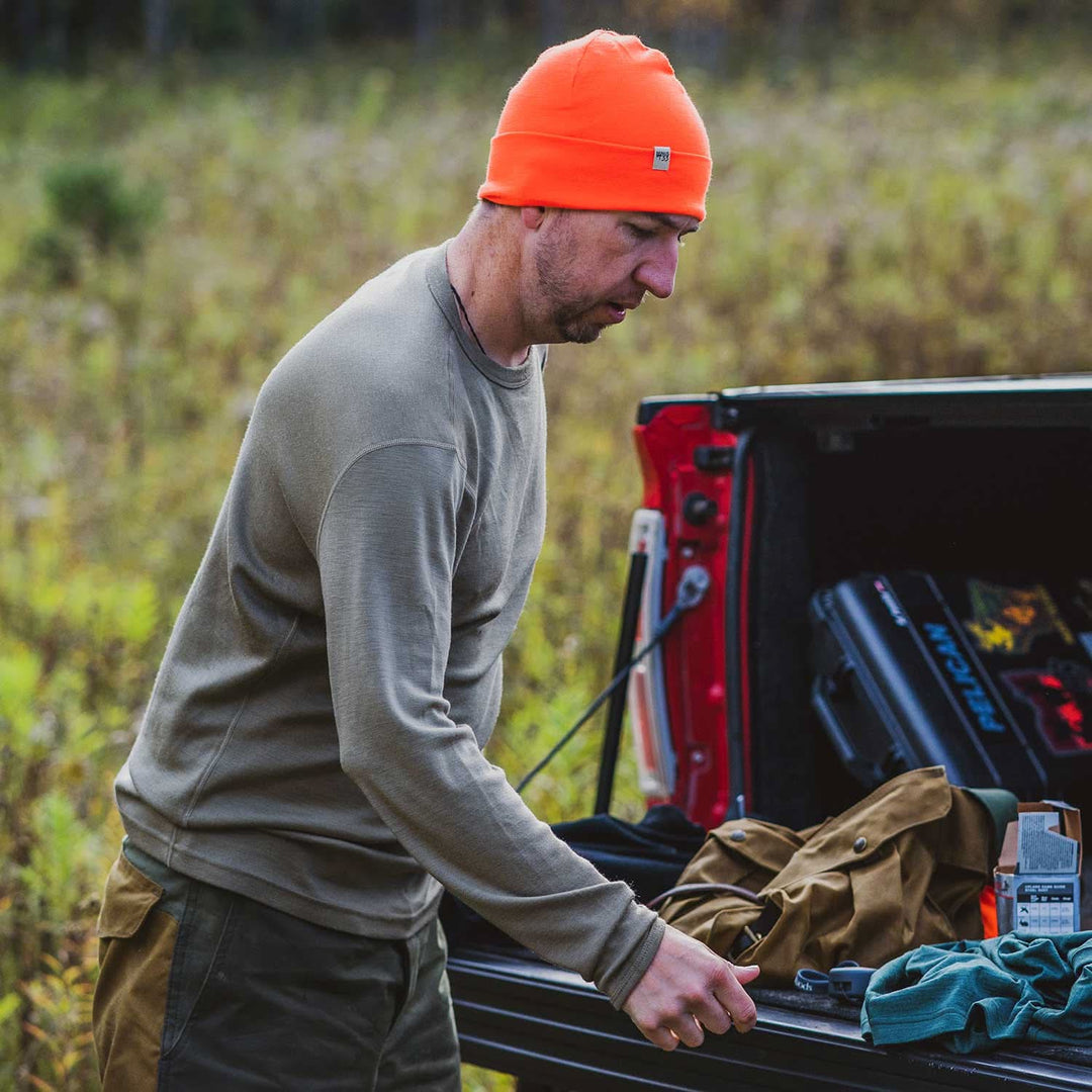 A man models a super soft, long sleeved merino wool thermal base layer crew. This top makes for a perfect first layer on a winter hike, or a nice casual wear on the chilly days of autumn and spring, front view beside a pickup truck 