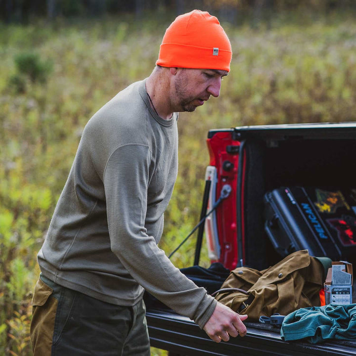 A man models a super soft, long sleeved merino wool thermal base layer crew. This top makes for a perfect first layer on a winter hike, or a nice casual wear on the chilly days of autumn and spring, front view beside a pickup truck 