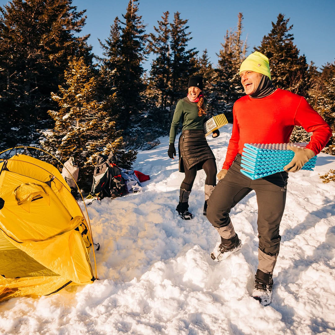 A man models a super soft, long sleeved merino wool thermal base layer crew. This top makes for a perfect first layer on a winter hike, or a nice casual wear on the chilly days of autumn and spring, front view at a campsite 