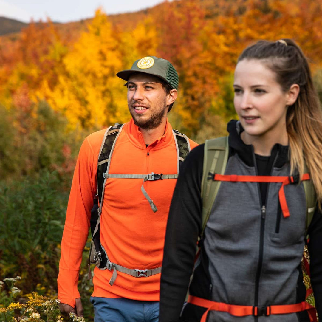 A man and woman hike through the fall foliage together. The man models the merino wool midweight quarter zip sweater, complete with flat-lock seams and thumbholes. 