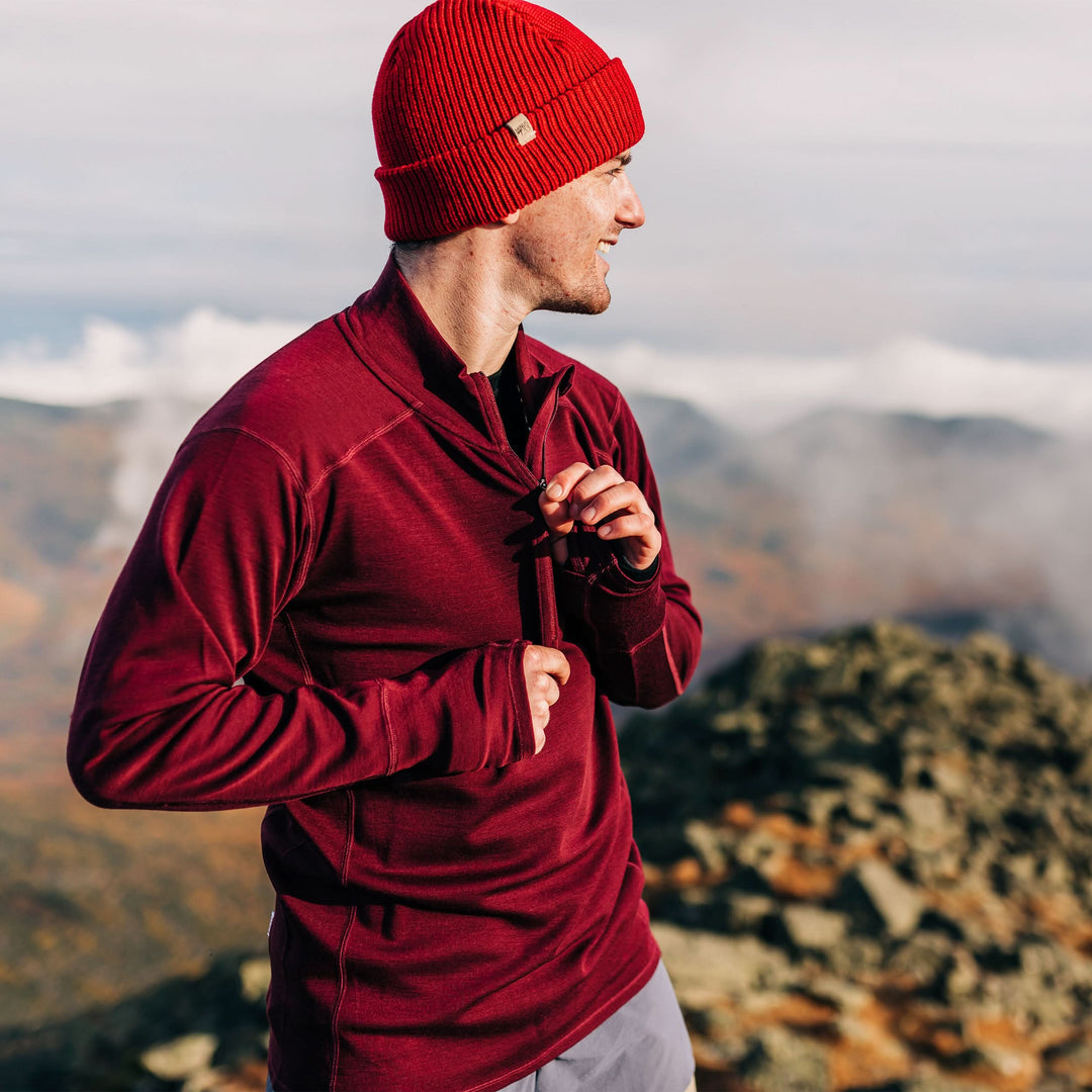 A man models the merino wool midweight quarter zip sweater, complete with flat-lock seams and thumbholes, studio front view 
