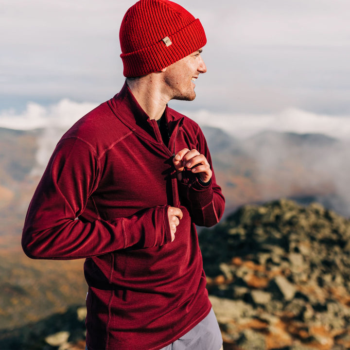 A man models the merino wool midweight quarter zip sweater, complete with flat-lock seams and thumbholes, studio front view 