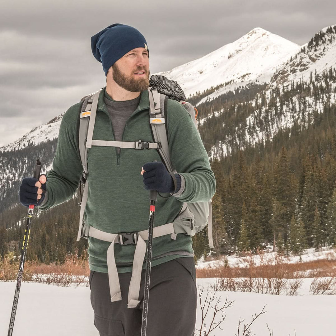 A man models the merino wool midweight quarter zip sweater, complete with flat-lock seams and thumbholes, front three-quarter view outdoors 
