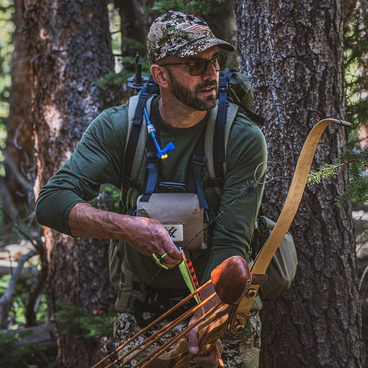 A man wears the lightweight long sleeved merino wool base layer crew neck top while hunting with a bow and arrow 