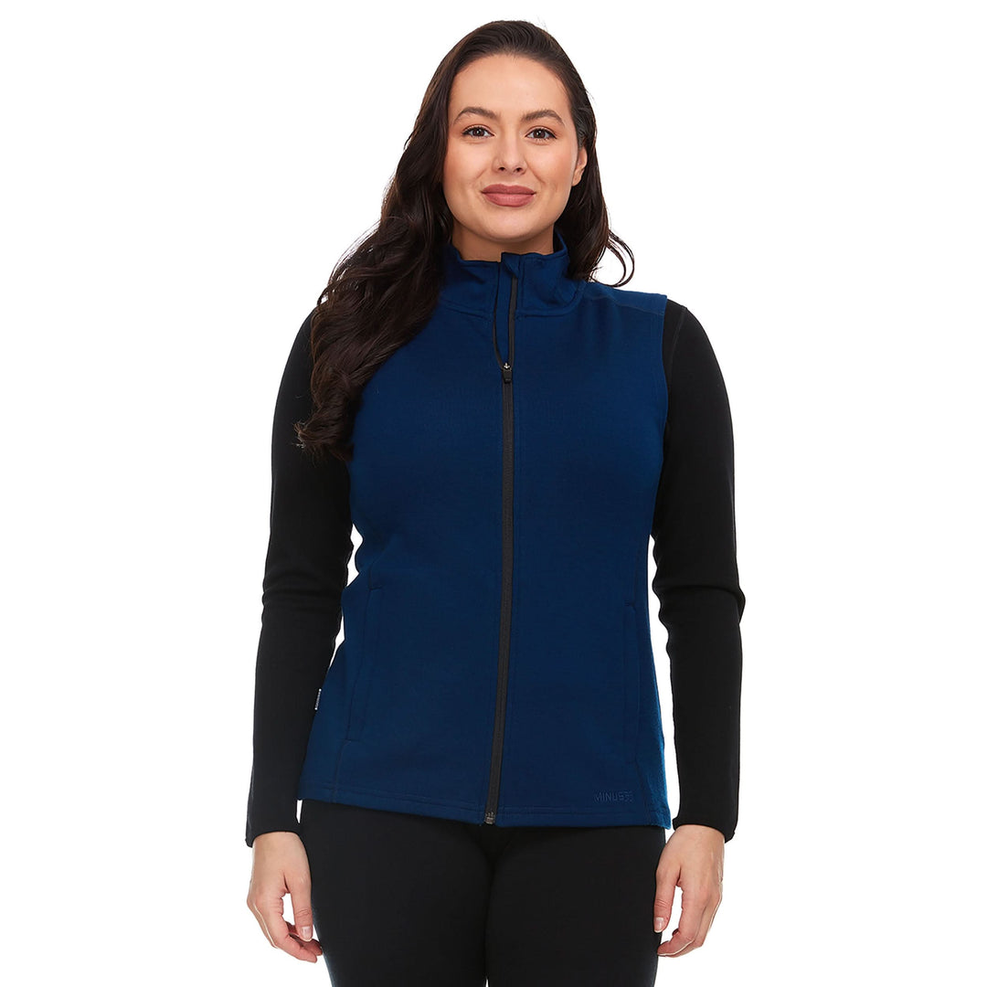 A woman models a hundred percent merino wool heavyweight full zip vest. This outer layer features a two and a half inch mock neck collar and two zippered pockets. Front view 1. #color_navy