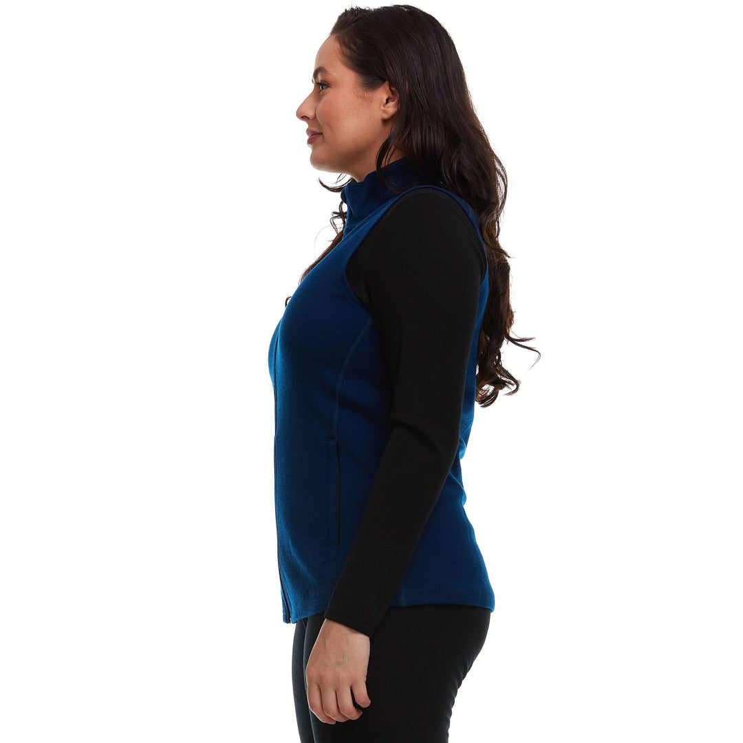 A woman models a hundred percent merino wool heavyweight full zip vest. This outer layer features a two and a half inch mock neck collar and two zippered pockets. 