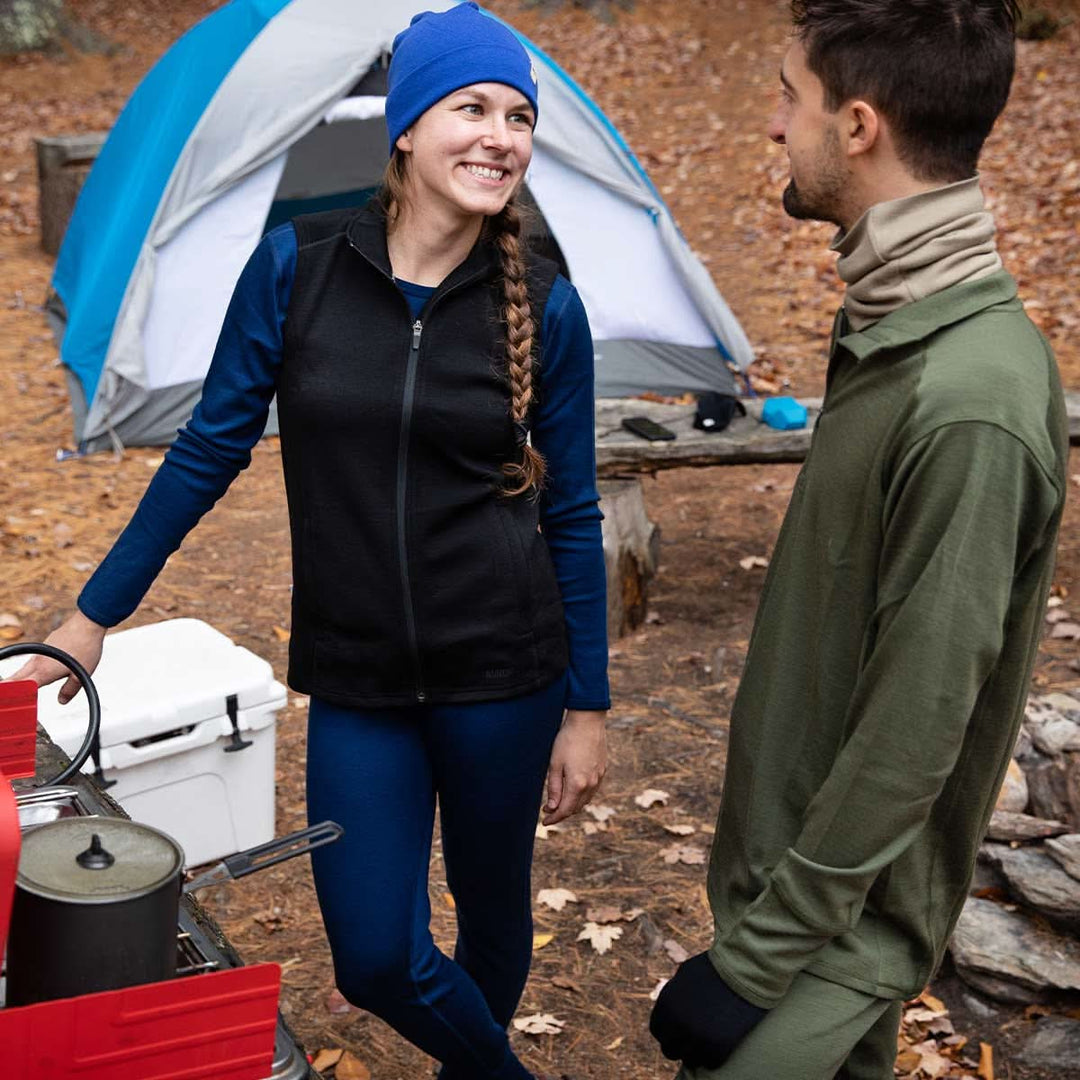 Two people chat in front of their tent and campsite. The woman wears a pair of one hundred percent merino wool midweight women&