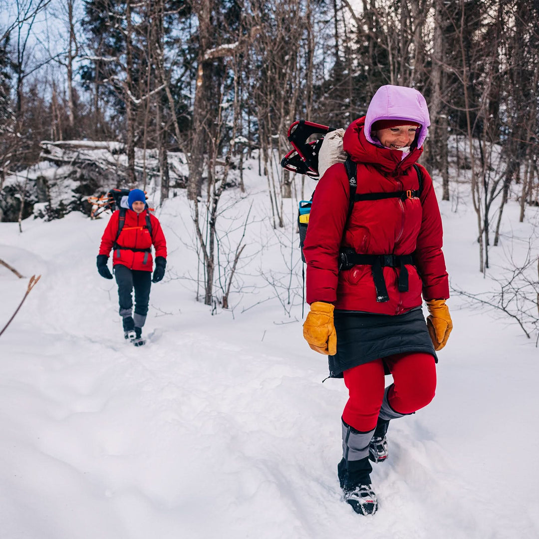 Two people hike a snowy trail in parkas and gloves. The woman in front is wearing a pair of one hundred percent merino wool midweight women&