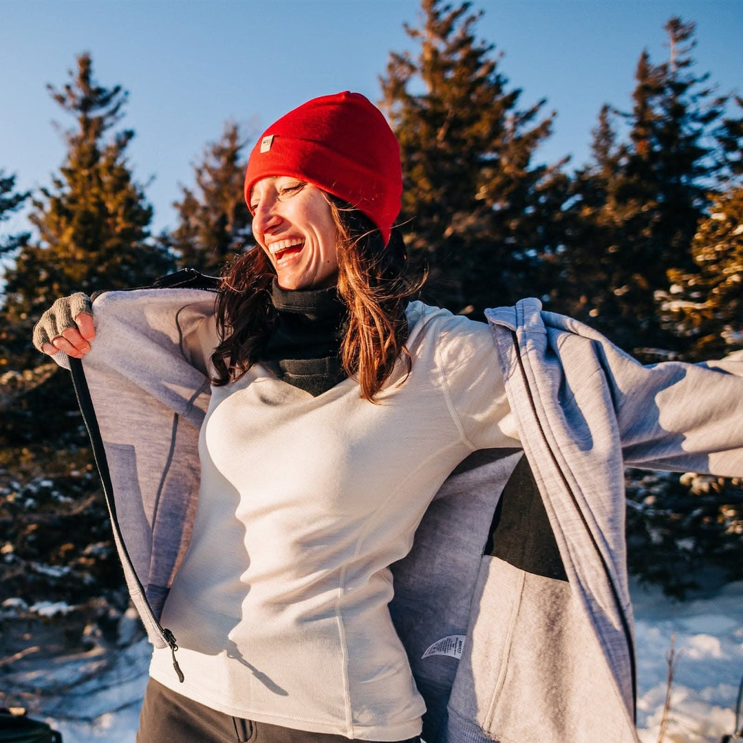 A woman smiles while adjusting her heavyweight merino wool hoodie. The woman is wearing a soft, 100% merino wool, midweight base layer crew top. The women&