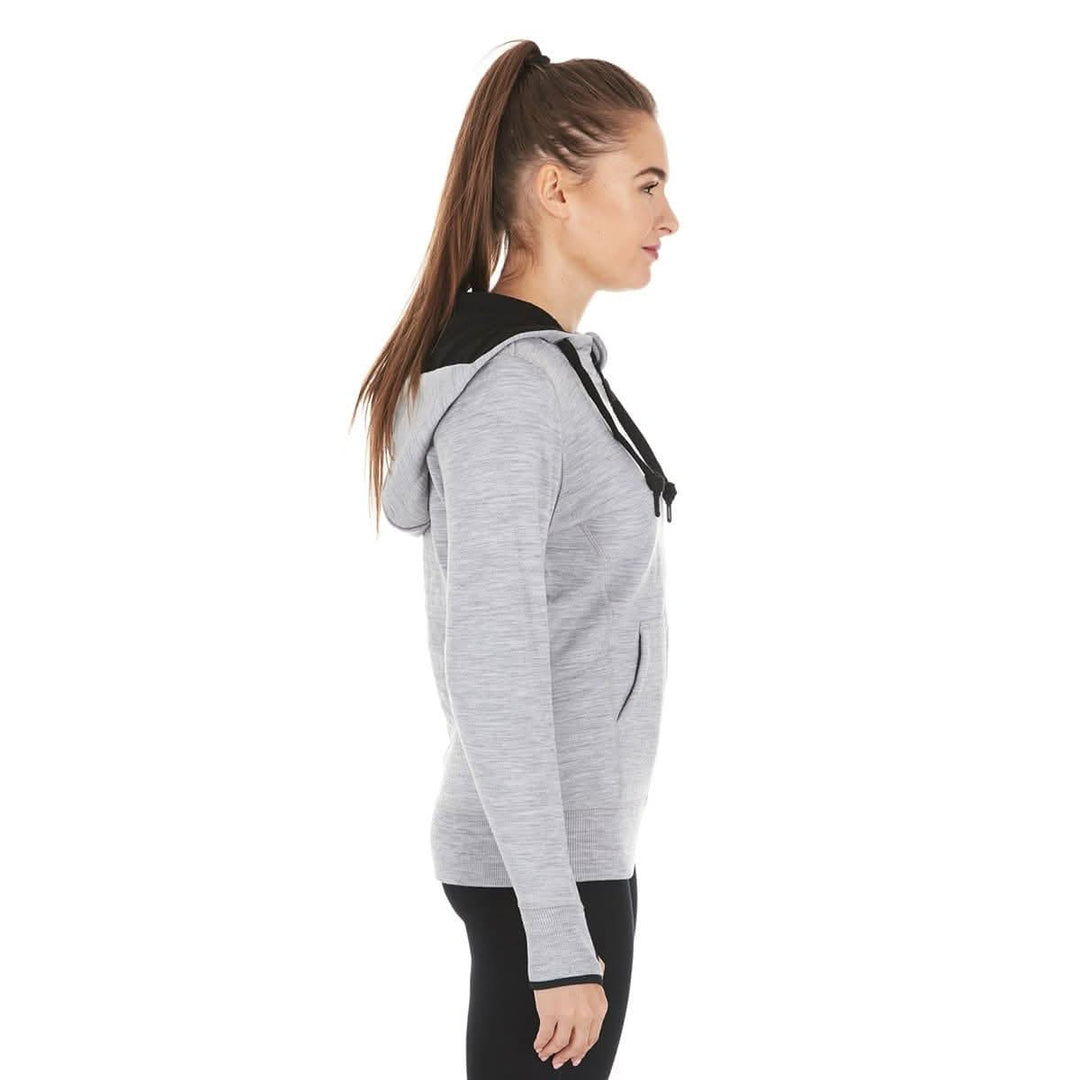 A woman models the heavyweight merino wool brushed fleece hoodie. The hoodie features a large hood with drawstrings, thumbholes, two pockets, and an interior stash pocket inside, right-facing side view 