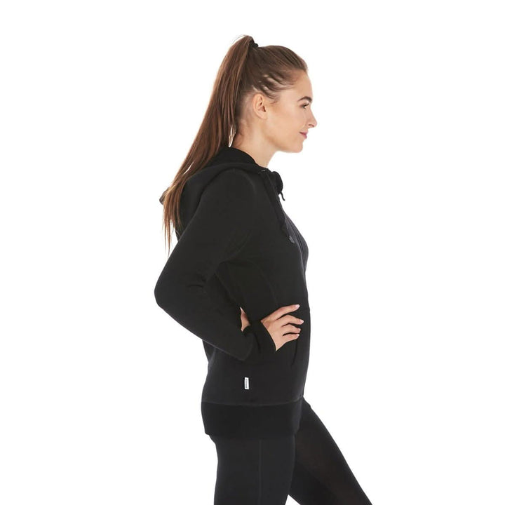 A woman models the heavyweight merino wool brushed fleece hoodie. The hoodie features a large hood with drawstrings, thumbholes, two pockets, and an interior stash pocket inside, right-facing side view 