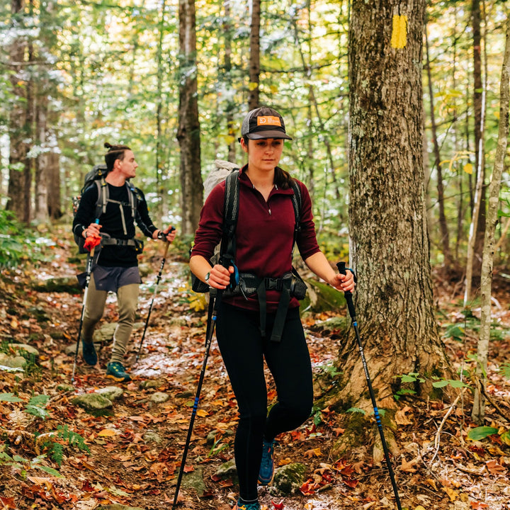 A woman hikes in the autumn woods wearing a soft midweight merino wool quarter zip sweater. The sweater features a 1/4 zip neckline and thumbholes at the cuffs 