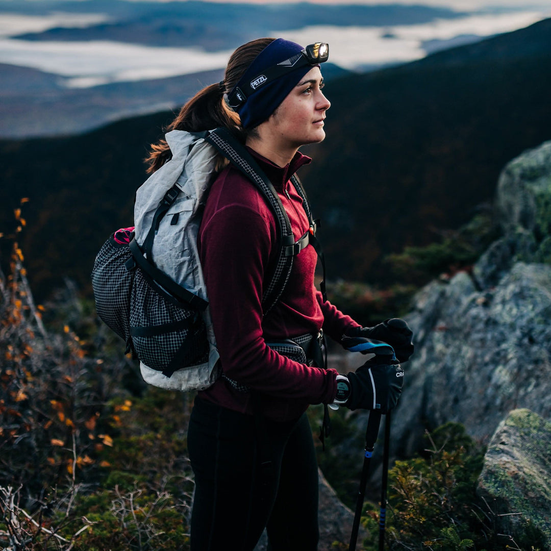 A woman stands on a mountain summit, enjoying the view in her soft midweight merino wool quarter zip sweater. The sweater features a 1/4 zip neckline and thumbholes at the cuffs 