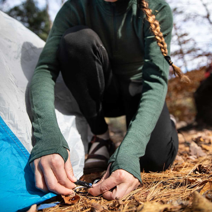 A woman kneels to stake her tent to the ground. The model is wearing the women&