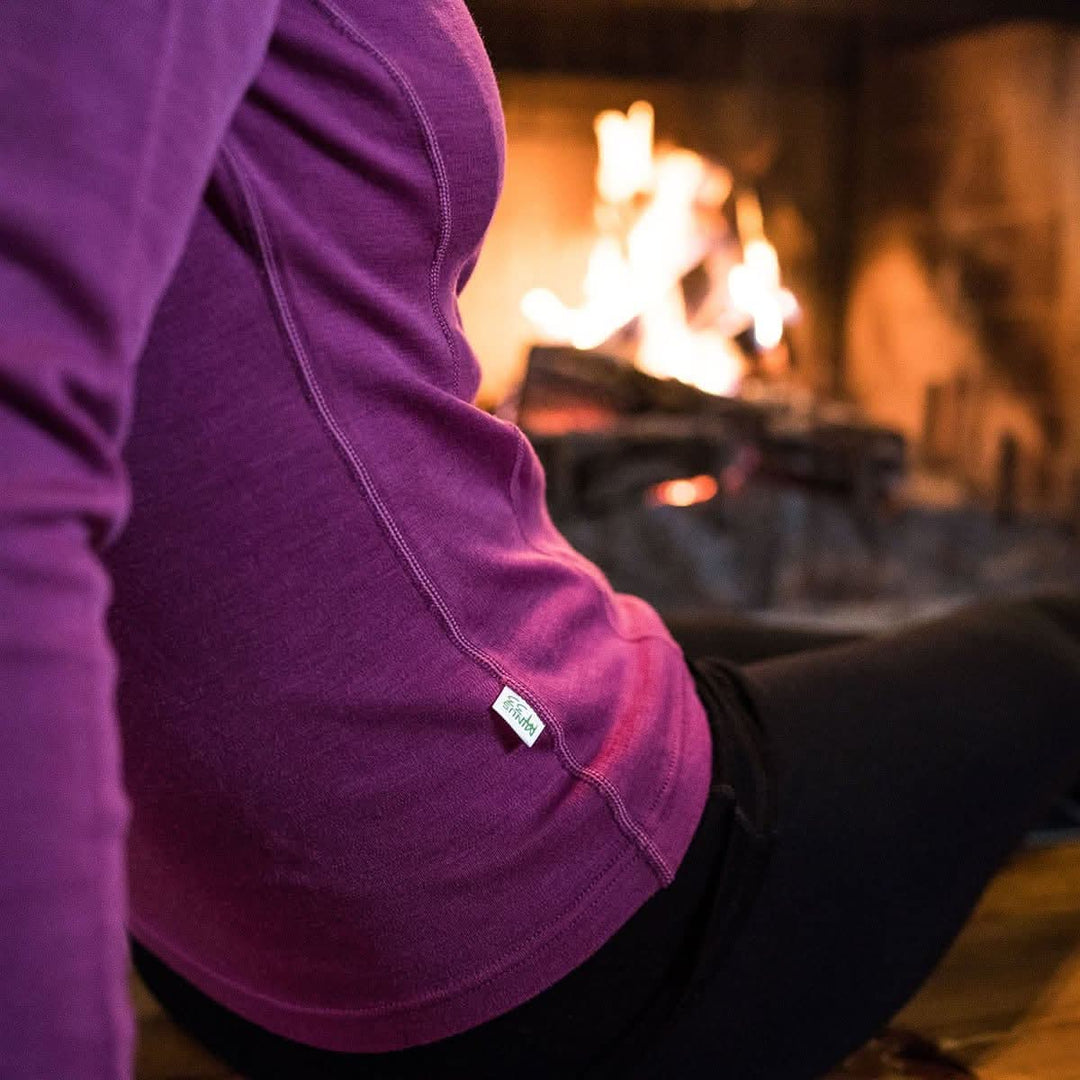 A person lounges next to a cozy fire. Close up on the flat-lock seams and princess paneling of the quarter zip sweater 