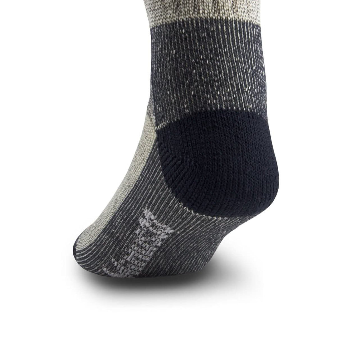Side close-up view of a denim heather merino wool day-hiker sock on a foot form, emphasizing the rounded navy reinforced heel, dark ribbed ankle and arch panels, and contrasting Minus33 logo near the forefoot 