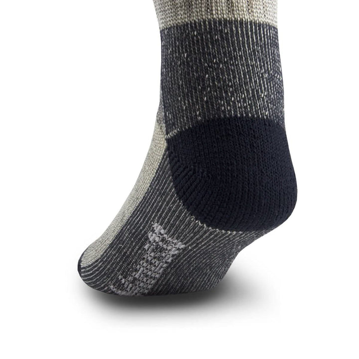 Side close-up view of a denim heather merino wool day-hiker sock on a foot form, emphasizing the rounded navy reinforced heel, dark ribbed ankle and arch panels, and contrasting Minus33 logo near the forefoot 