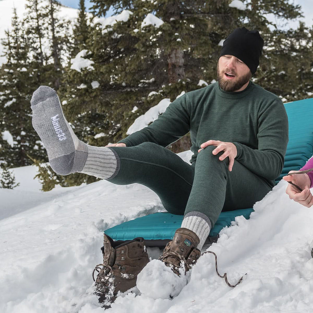Midweight - Day Hiker Crew Socks - Minus33 Merino Wool Clothing, man showing a raised gray socked foot while seated in snow
