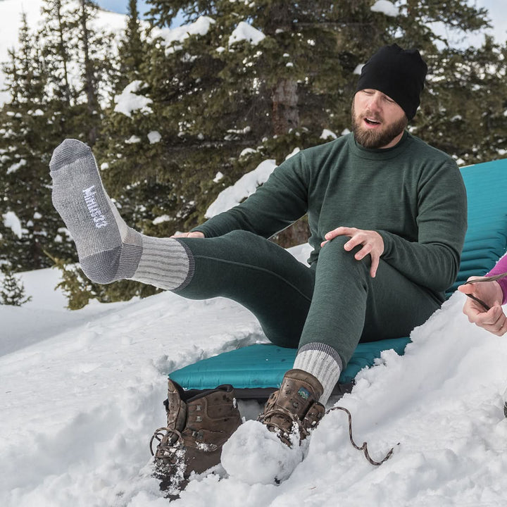 Midweight - Day Hiker Crew Socks - Minus33 Merino Wool Clothing, man showing a raised gray socked foot while seated in snow