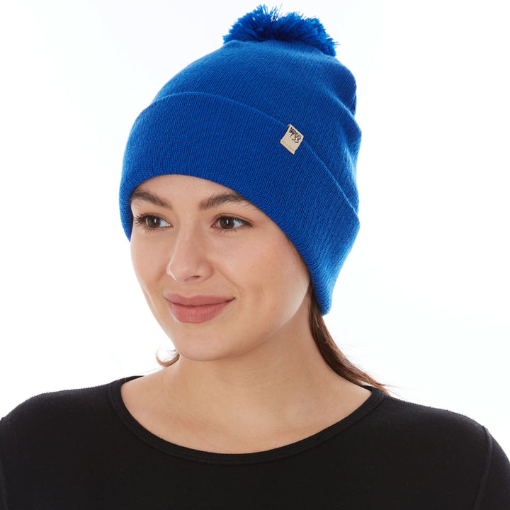 Close-up front left three-quarter view of a woman wearing a royal blue midweight merino wool cuffed beanie with a matching pom-pom and a small Minus33 logo patch on the folded brim 