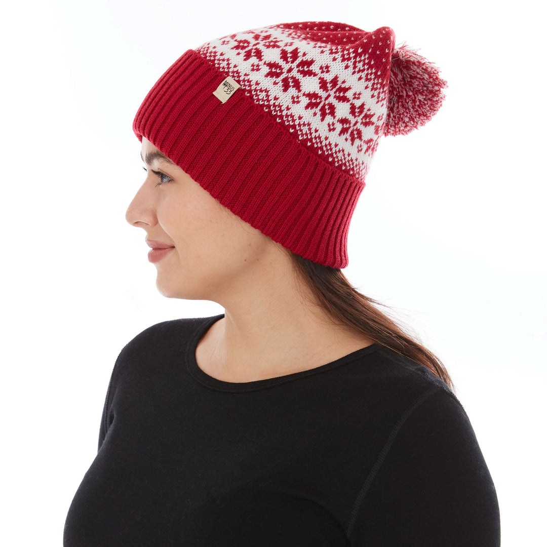 Close-up left side profile view of a woman wearing a true red midweight merino wool cuffed beanie with a natural cream snowflake knit pattern, logo patch, and red-and-cream pom-pom 