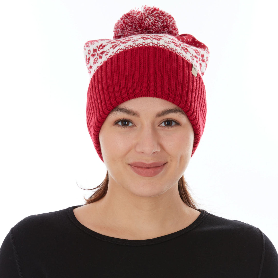 Close-up straight-on front view of a woman wearing a true red midweight merino wool cuffed beanie with a natural cream snowflake band and a red-and-cream pom-pom 
