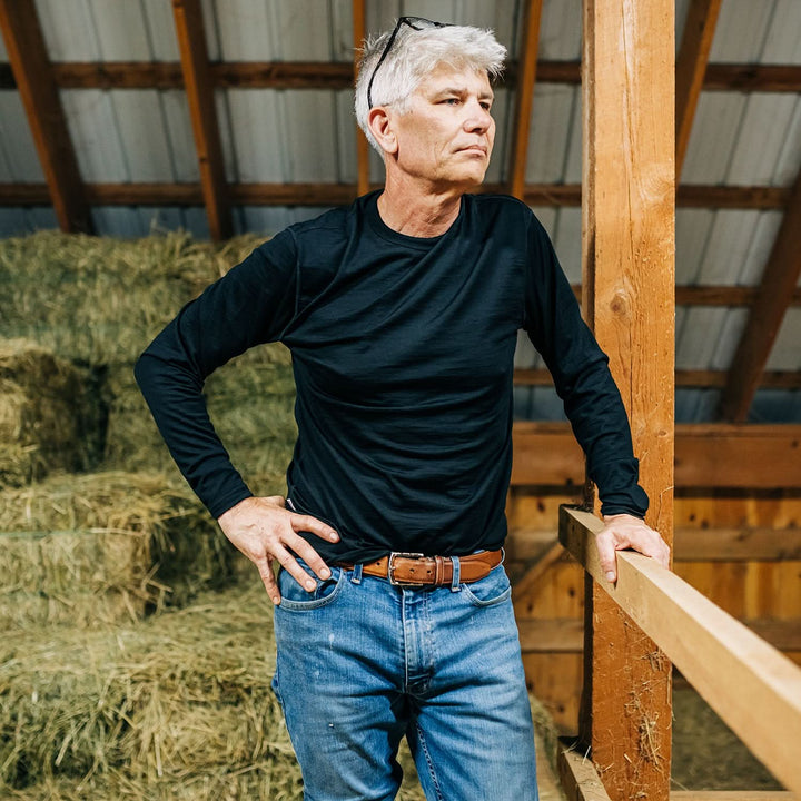 Man stands in hay loft wearing black long sleeve merino shirt 
