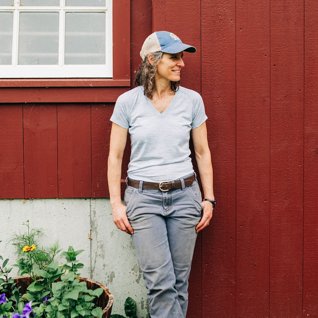 Woman wearing microweight merino wool v-neck stands against barn 