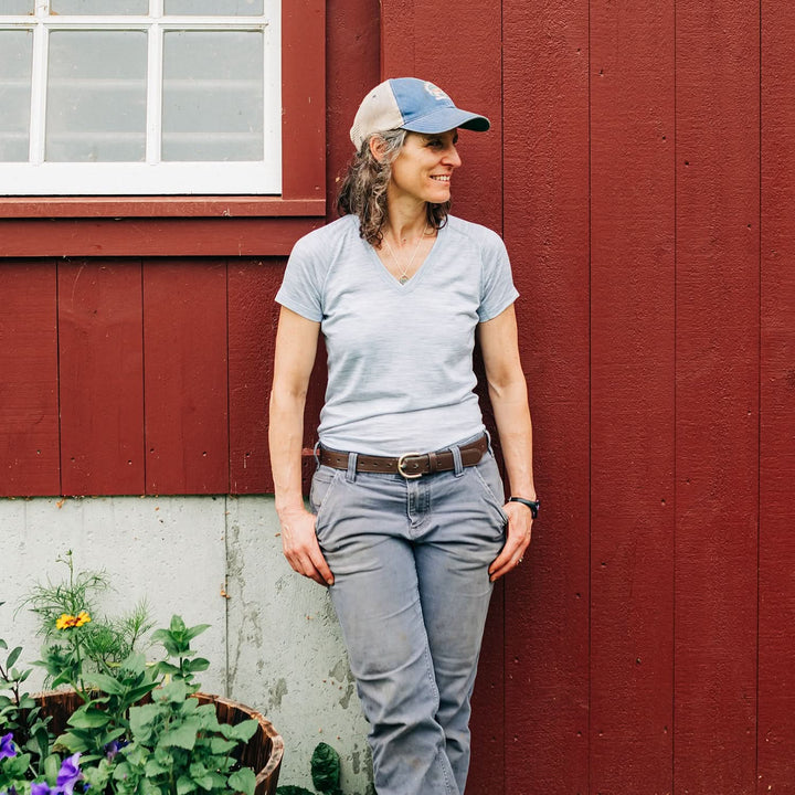 Woman wearing microweight merino wool v-neck stands against barn 