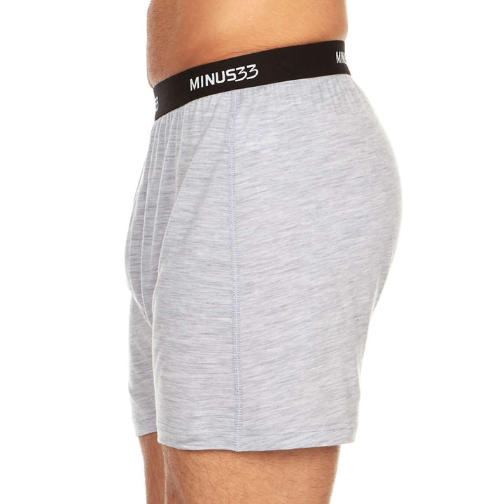 Left side view from waist to mid-thigh of a man wearing ash gray Woolverino micro weight merino wool boxer shorts, showing the elastic waistband, relaxed side panel, curved hem, and loose leg opening 