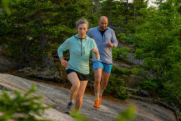 Two runners in merino tops jogging along a forest trail
