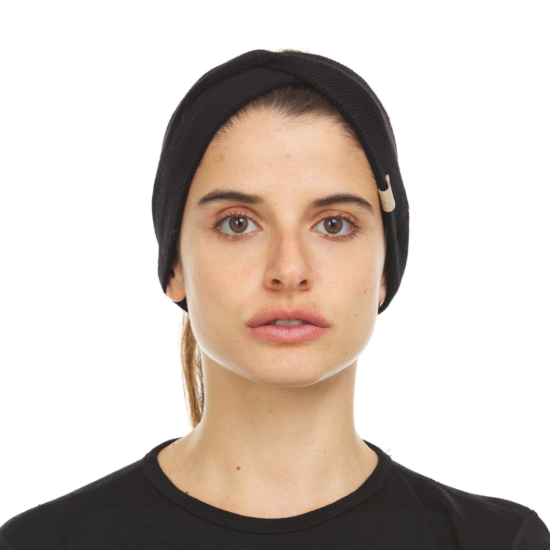 Front view of a black midweight merino wool knit headband laid flat on a white background, showing the wide ear-covering band, centered twisted knot, ribbed texture, and tapered back 