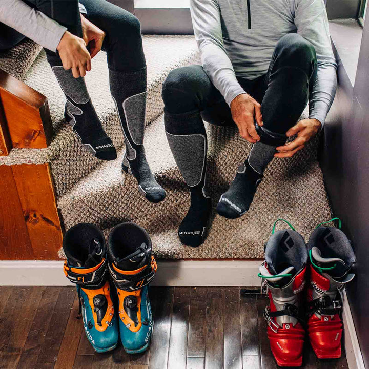 Front three-quarter view of black micro weight merino wool light-cushion over-the-calf snowboard socks being worn, showing tall cuffs, padded shin panels, supportive ankles, and reinforced toes 