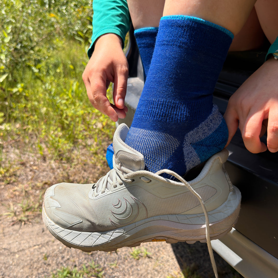 A runner in blue merino wool socks puts on their shoe 