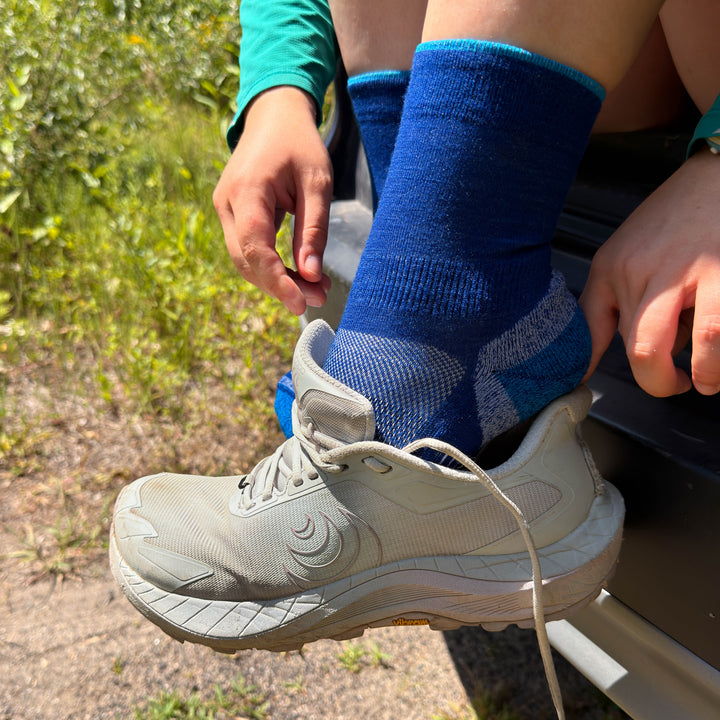 A runner in blue merino wool socks puts on their shoe 