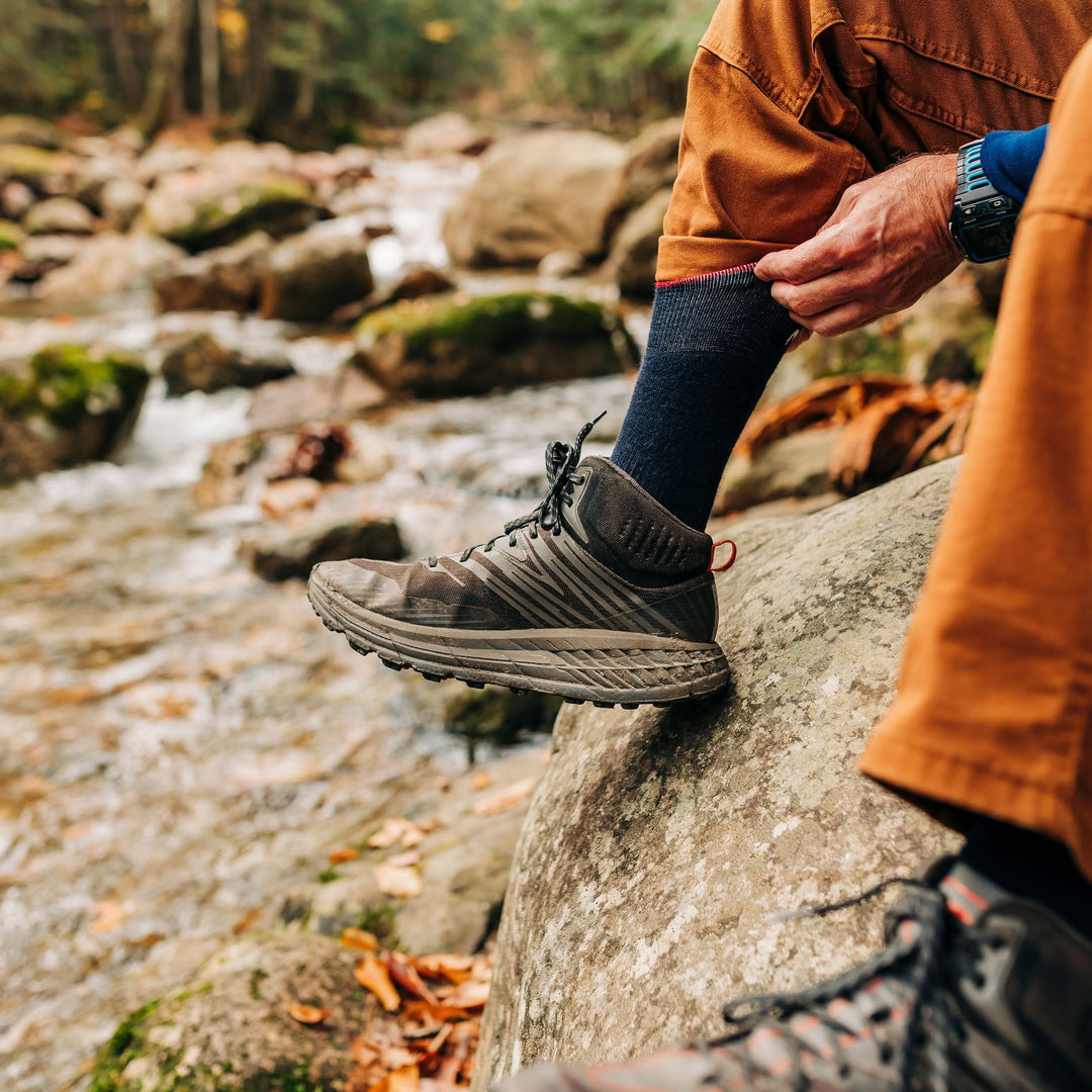 NH USA Made lightweight merino wool crew socks, man lifting a pant cuff above a black sock beside a stream 