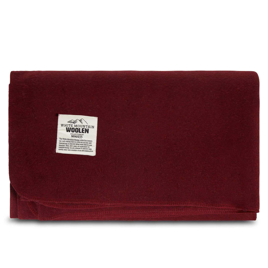Front view of a solid burgundy lodge wool blanket folded into a rectangle, showing the stitched lower edge and White Mountain Woolen Mill label near the upper left 