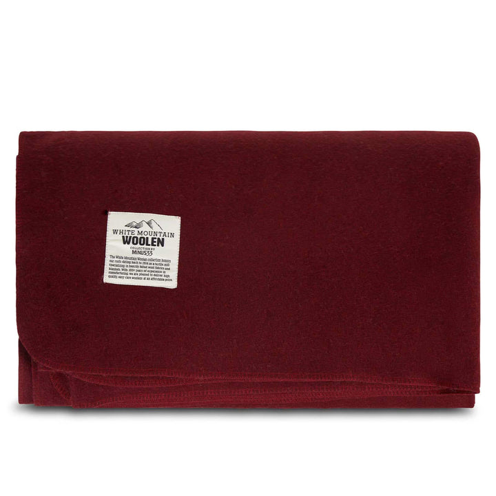 Front view of a solid burgundy lodge wool blanket folded into a rectangle, showing the stitched lower edge and White Mountain Woolen Mill label near the upper left 