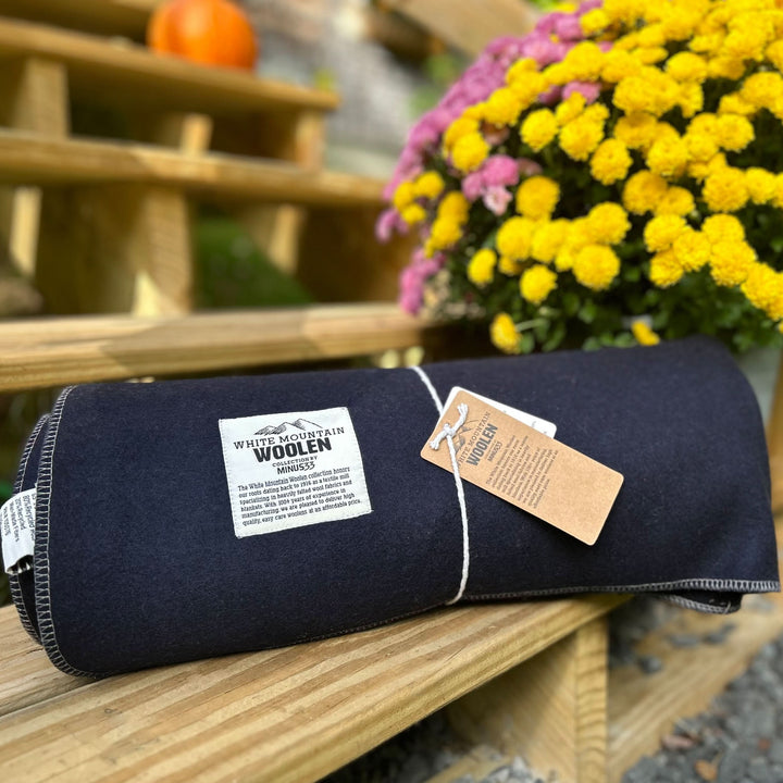 Lodge twin wool blanket, rolled on a wooden bench beside flowers with tag visible 