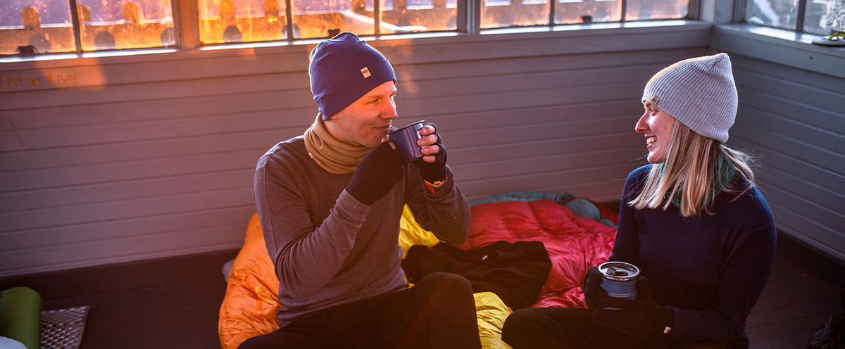 Two people sitting inside a cabin and drinking from cups.