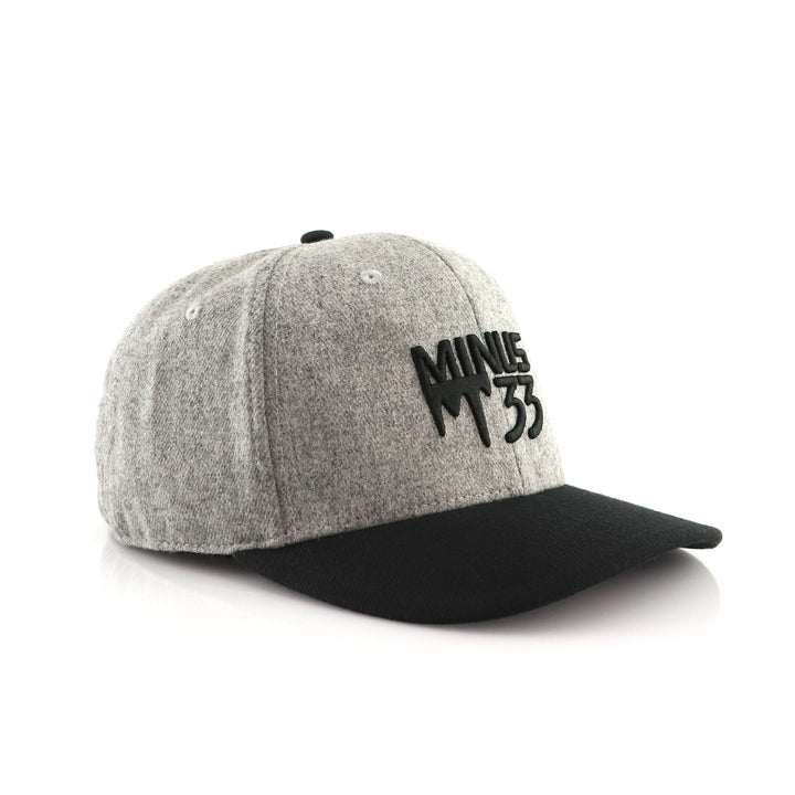 Three-quarter front view of a gray heather baseball cap with a curved bill, structured crown, embroidered green M33 mountain logo, and visible top button and panel seams 