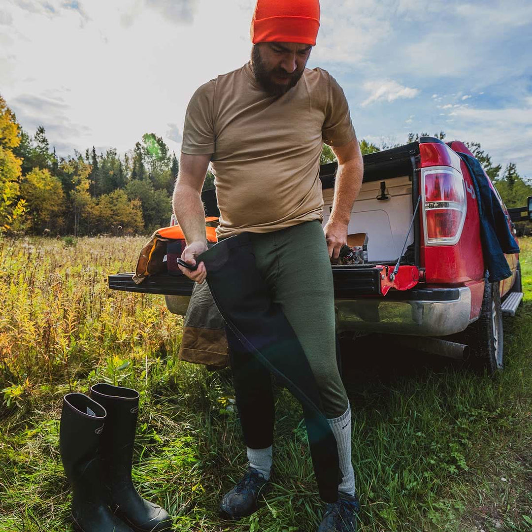 man out hunting putting on his zip up bottoms over base layer bottoms 