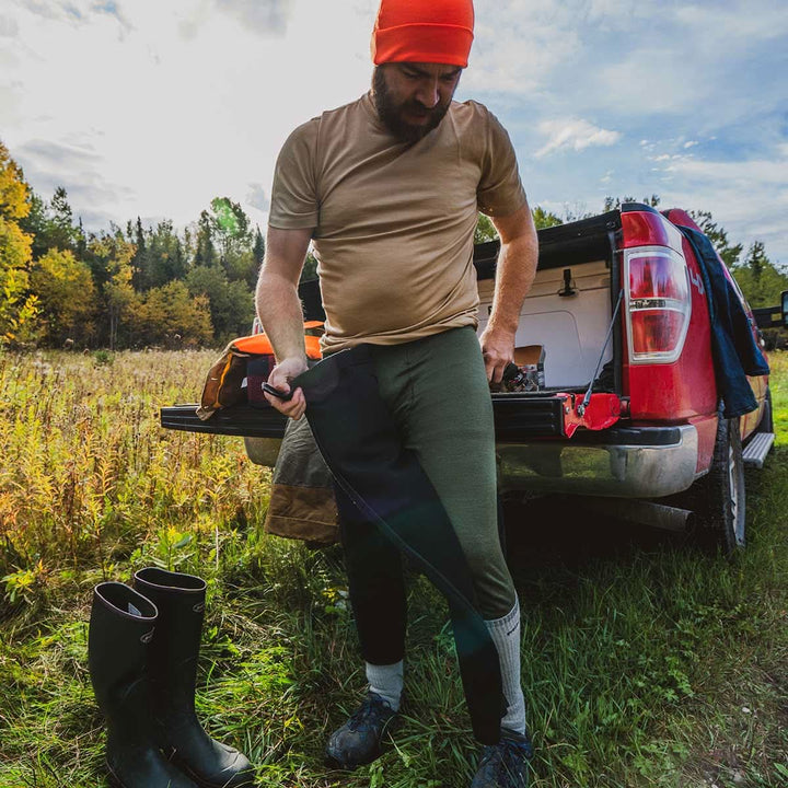 man out hunting putting on his zip up bottoms over base layer bottoms 