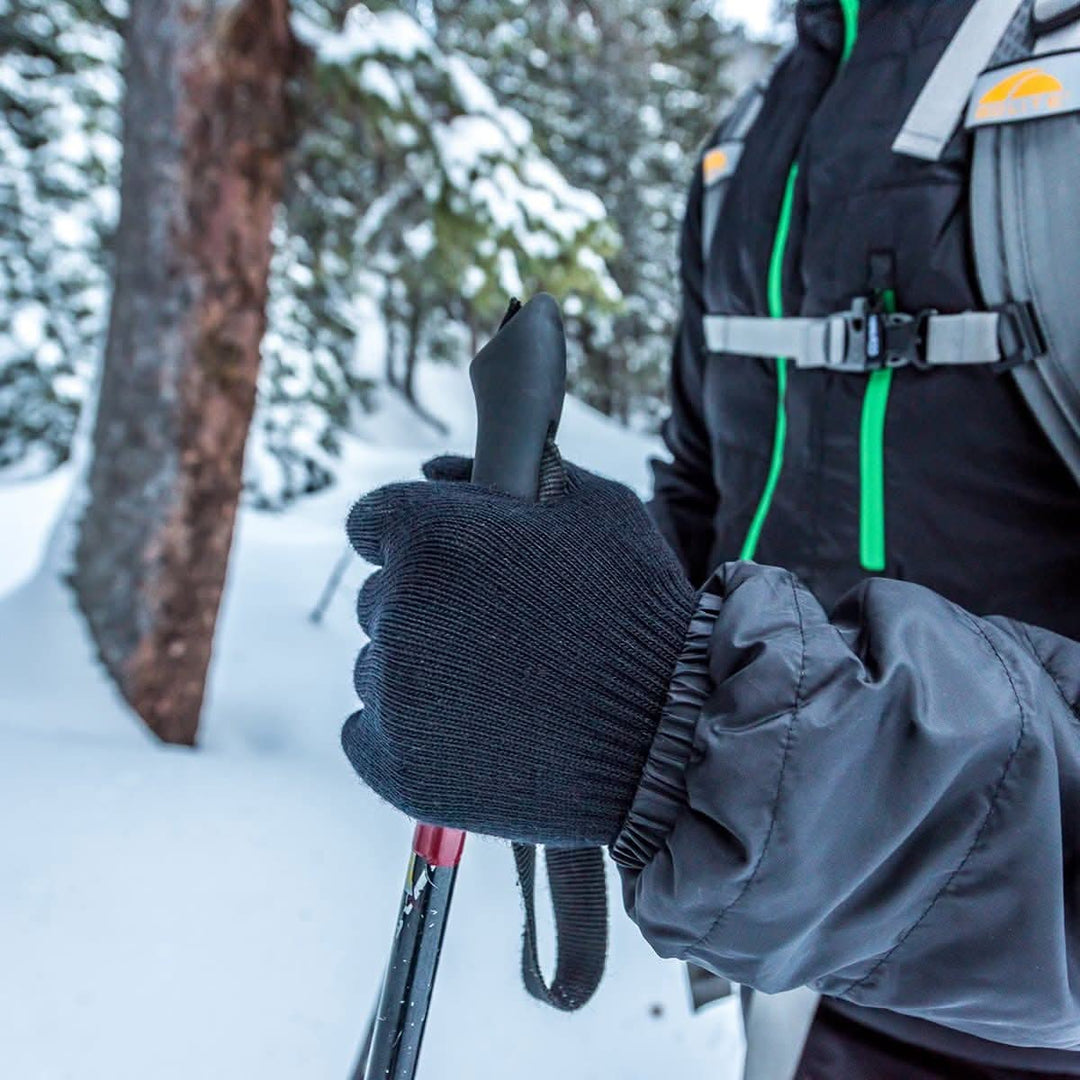 Close-up of lightweight merino glove liners gripping ski poles 
