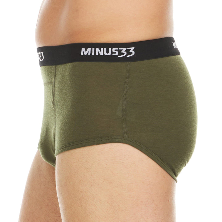 Left side view from waist to upper thighs of a man wearing olive drab green Woolverino micro weight merino wool briefs, showing the elastic waistband, smooth side panel, high-cut leg opening, and close fit 