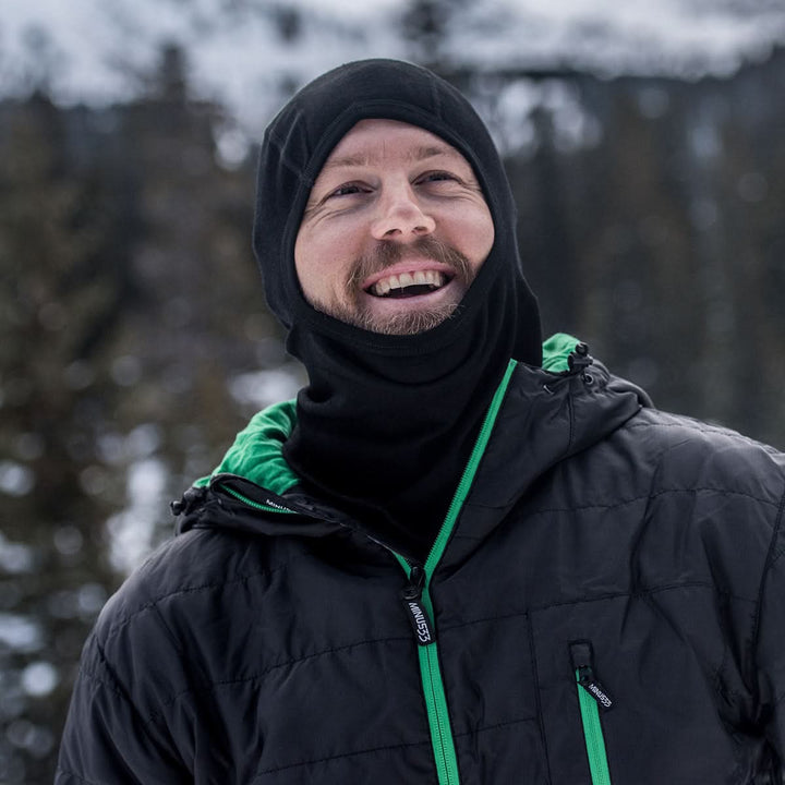 man wearing a black expedition weight balaclava while outside in the winter, front view 