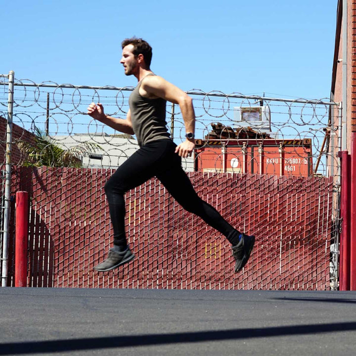 Full front view from waist to ankles of a man wearing black Woolverino midweight merino wool flyless running tights, showing the wide waistband, smooth front, fitted full-length legs, and ankle cuffs 