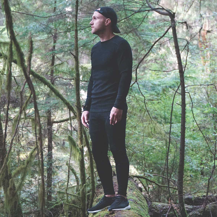 Close-up front view from waist to upper thighs of a man wearing black Woolverino midweight merino wool flyless running tights, showing the wide waistband, smooth front panel, flatlock seams, and close-fitting legs 