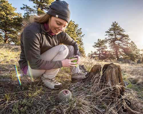 woman hiking and looking at plants while wearing merino wool mid layer and beanie