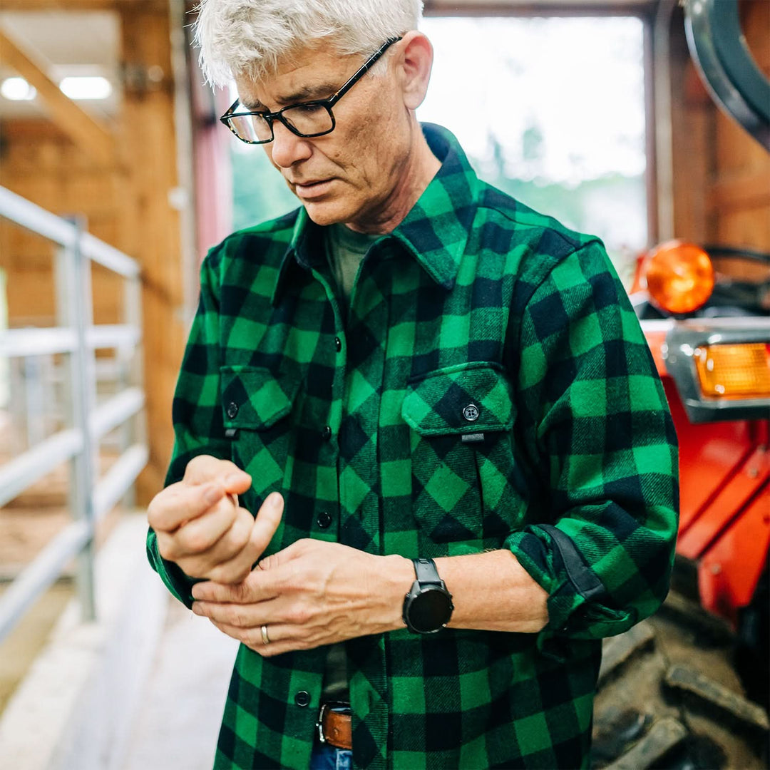 Man buttons green plaid heavyweight wool shirt in barn 
